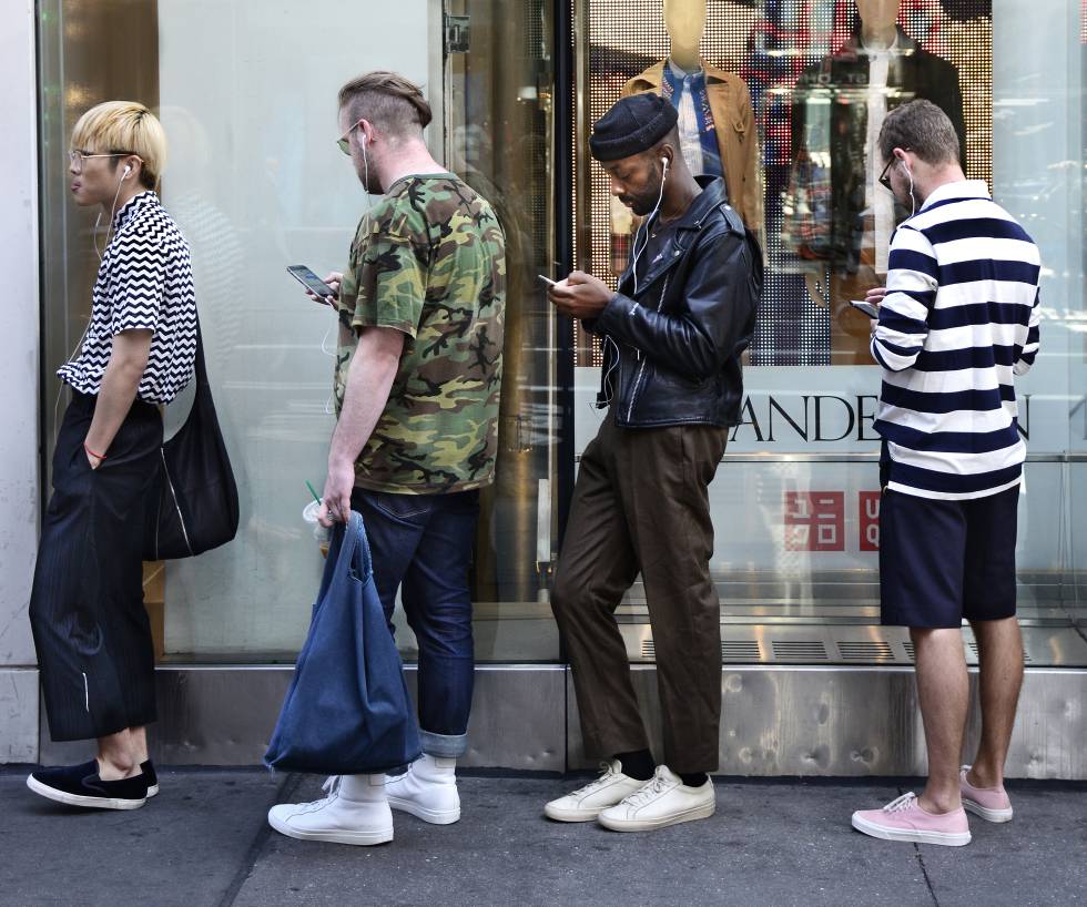 Tres jóvenes usan sus móviles mientras hacen cola para entrar en un establecimiento Uniqlo, en Nueva York.